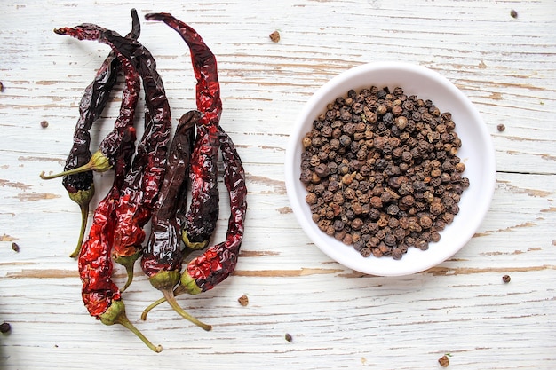 Free Photo black peppercorns on small white plate on white wooden table with dried black chili peppers, top view, spices