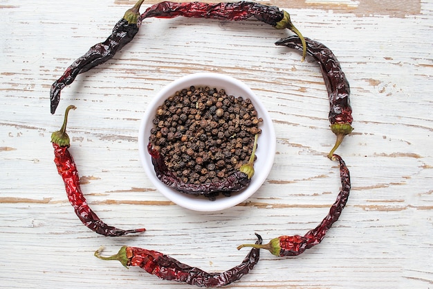 Free Photo black peppercorns on small white plate on white wooden table with dried black chili peppers, top view,