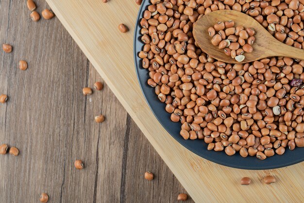 A black plate full of dried raw red beans with wooden spoon.