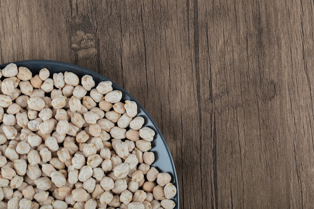 Free photo a black plate full of dried raw white peas on wooden table .