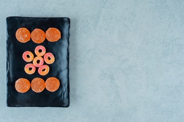 Free photo a black plate full of round orange jelly sweets in the shape of rings and orange jelly candies with sugar