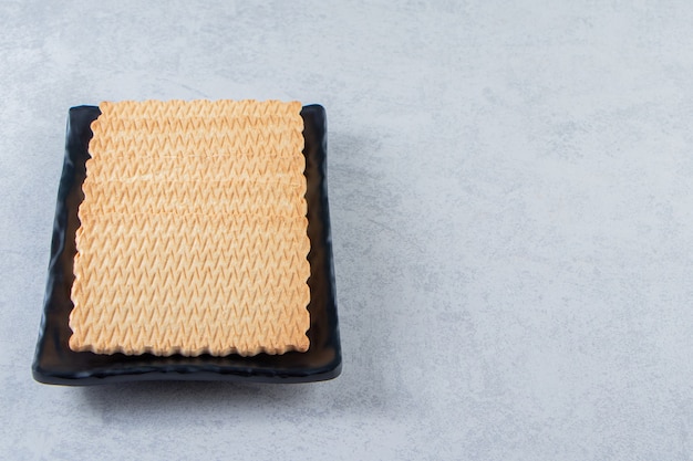 Black plate of tasty biscuits placed on stone background.