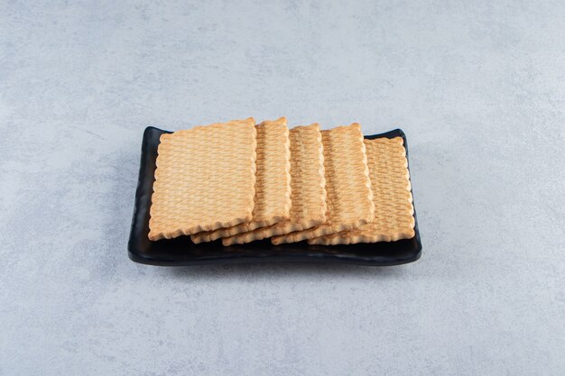 Black plate of tasty biscuits placed on stone background.