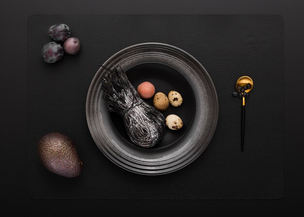 Black plate with black pasta and quail eggs on a dark background