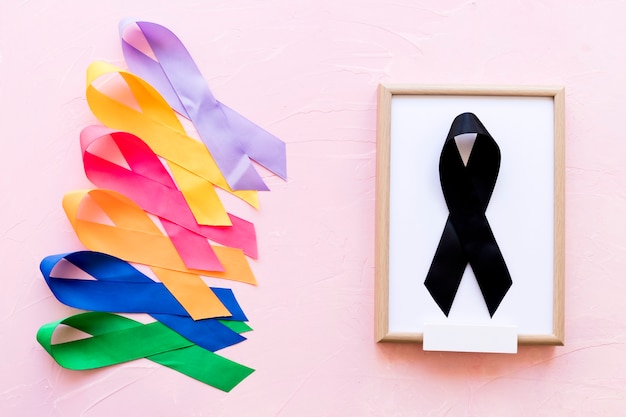 Free photo black ribbon on white wooden frame near the row of colorful awareness ribbon