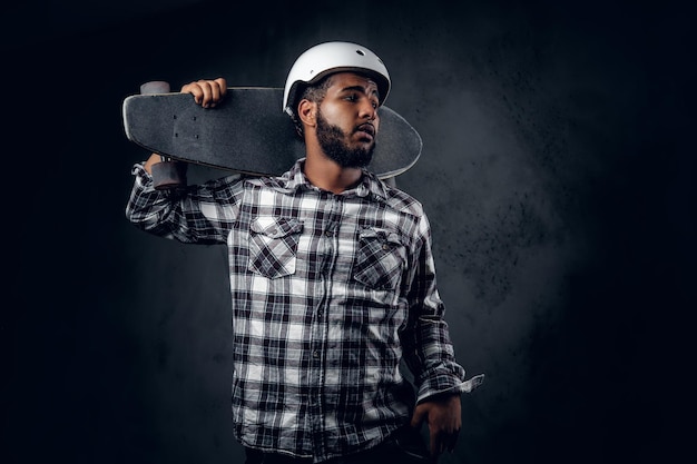 Free Photo black skater dressed in a fleece shirt holds long board over grey background in a studio.