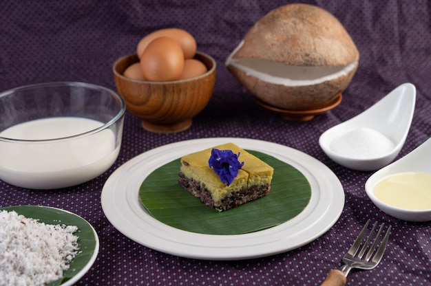 Free photo black sticky rice and custard on a banana leaf in a white plate with butterfly pea flowers.