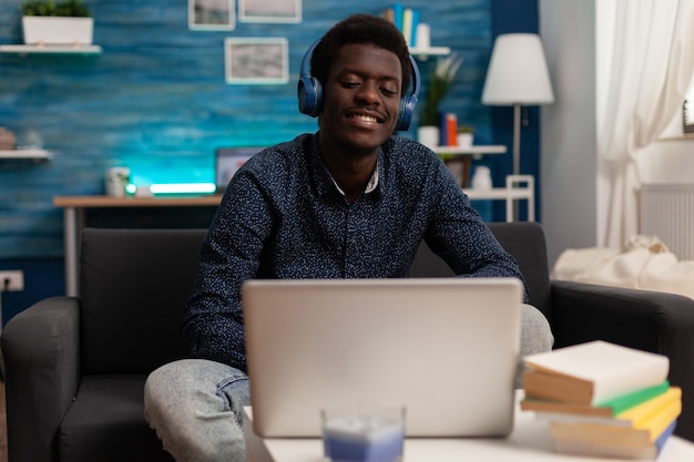 Black student wearing headphone having audio business course on laptop