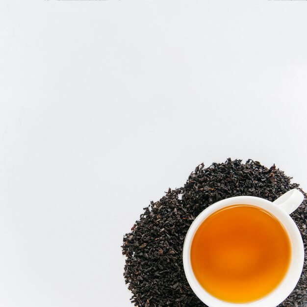 Black tea cup over the dried black leaves isolated on white backdrop