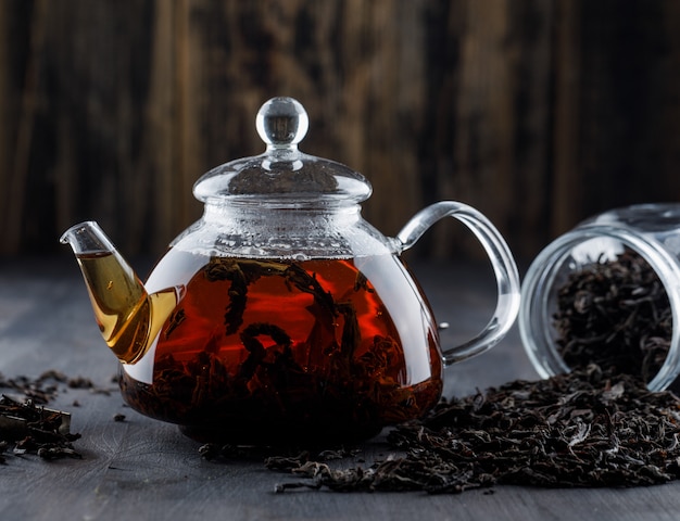 Black tea with dry tea in a teapot on wooden surface, side view