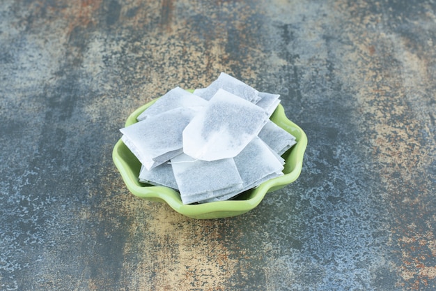 Black teabags in green bowl on marble background.