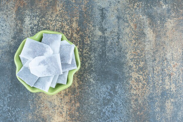 Black teabags in green bowl on marble background.