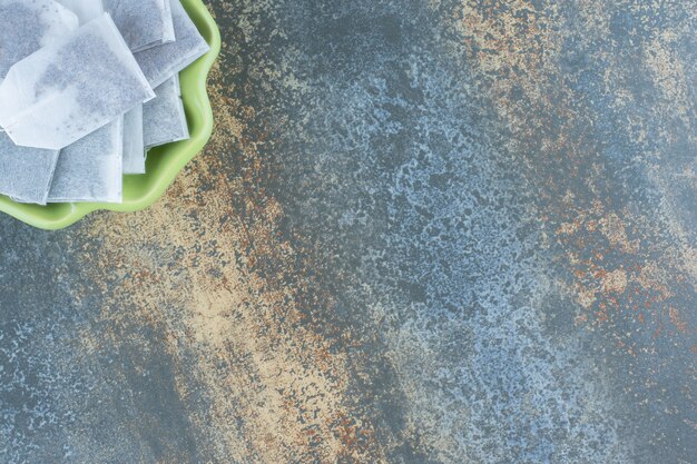 Black teabags in green bowl on marble table.