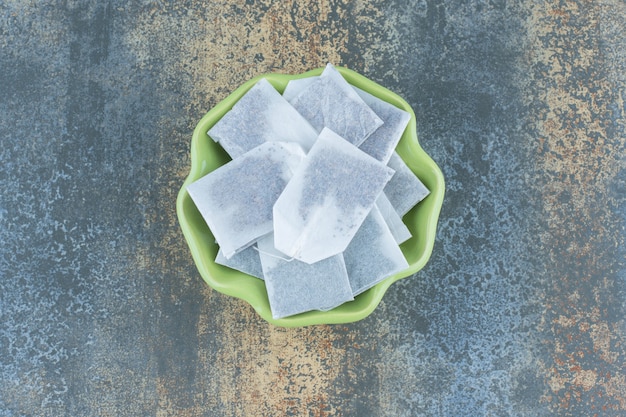 Black teabags in green bowl on marble.