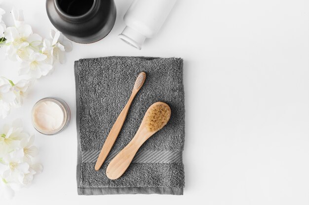 Black towel; brush; moisturizing cream; flowers and container on white background