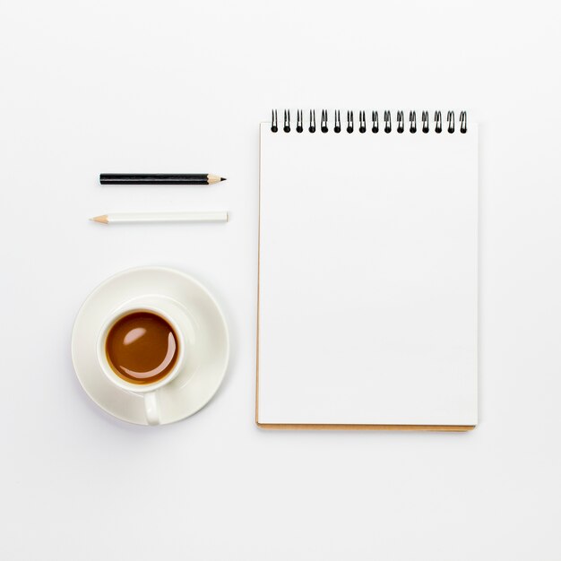 Black and white pencils with coffee cup and blank spiral notepad on office desk