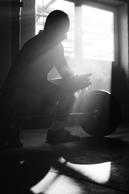 Free photo black and white photo of a sportsman using talcum powder on his hands and preparing for weight training in a gym