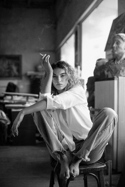 Free photo black and white portrait of beautiful woman posing indoors while smoking a cigarette