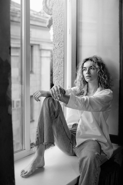 Free Photo black and white portrait of beautiful woman posing indoors on a windowsill