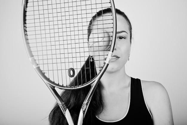 Free photo black and white portrait of beautiful young woman player in sports clothes holding tennis racket while standing against white background