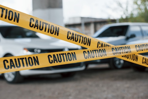 Black and white vehicles. Yellow caution tape near the car parking lot at daytime. Crime scene