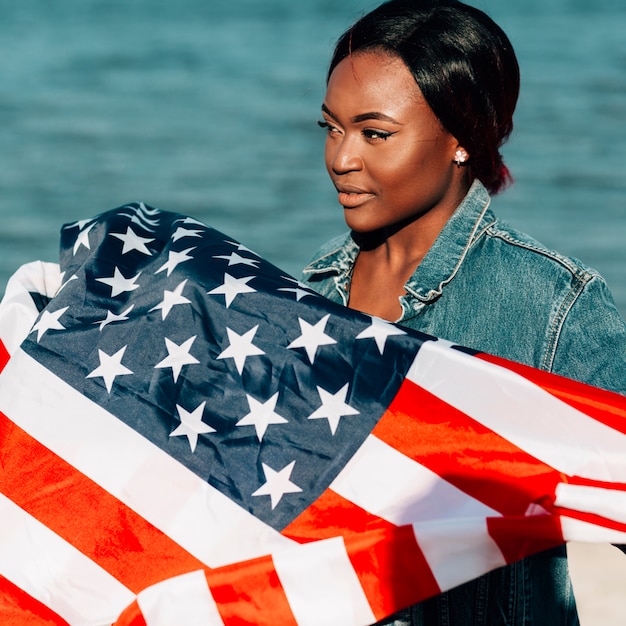 Free photo black woman standing and holding american flag