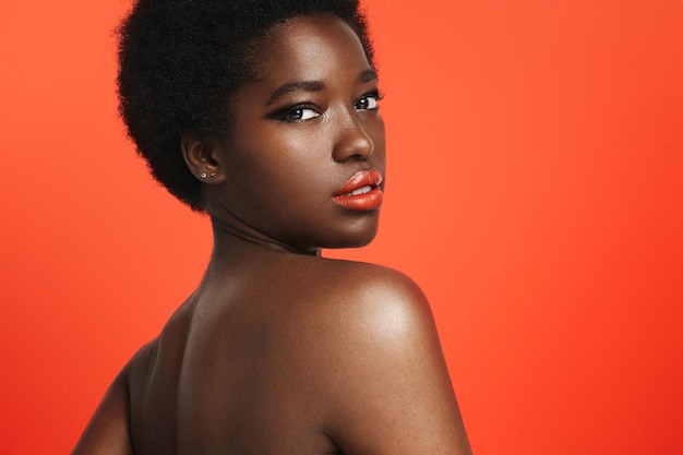 Black woman wearing bright lips on a bright orange background