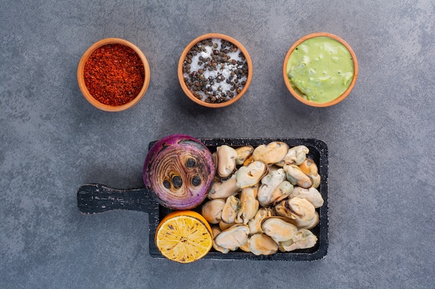 Free Photo a black wooden board of cooked shells with fried onion and sliced lemon on a stone background.