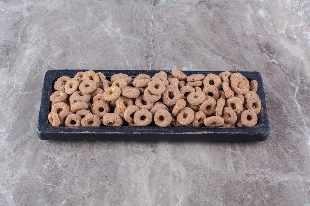 A black wooden board of healthy chocolate cereal rings for breakfast .