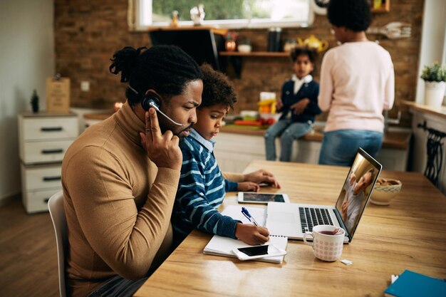 Black working father making a conference call while son is sitting in his lap at home