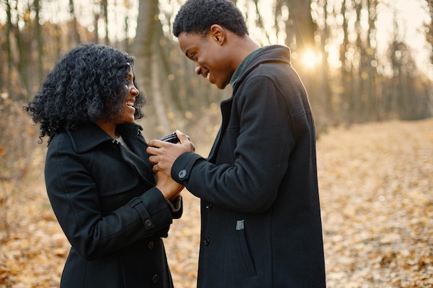 Free photo black young man and his girlfriend holding in hands one coffee cup. romantic couple walking in autumn park. man and woman wearing black coats.