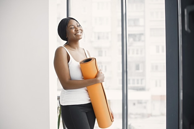 Black young woman ready for workout holding orange yoga mat