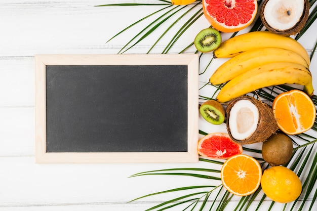 Free photo blackboard near plant leaves with fresh tropical fruits