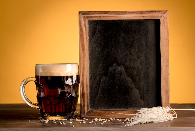 Free Photo blackboard standing next of glass of beer on wooden table 