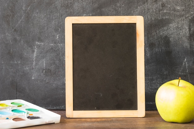 Free photo blackboard on table with paints and apple