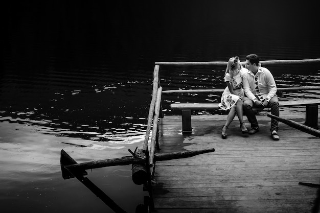 Free photo blakc and white picture of young people kissing on bench over the lake