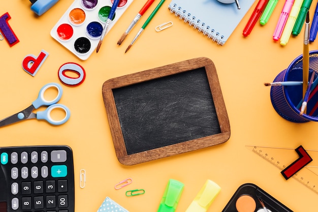 Free photo blank blackboard surrounded with school supplies scattered on yellow desk