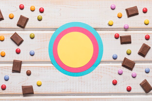 Blank blue; pink and yellow circular frame with confectionery on wooden desk