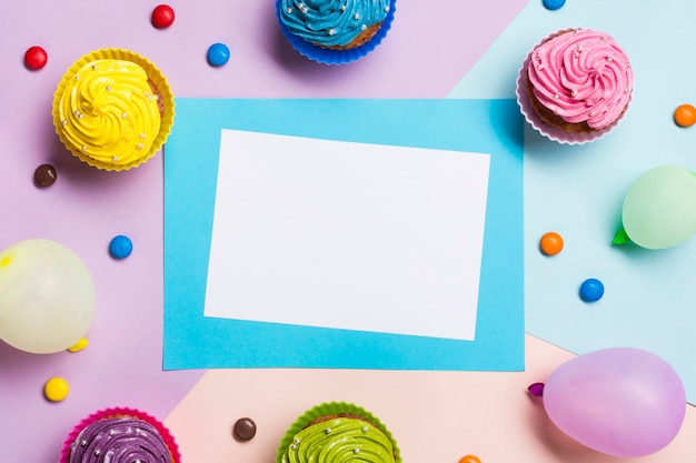 Blank blue and white card surrounded with balloon; muffins and gems on colored backdrop