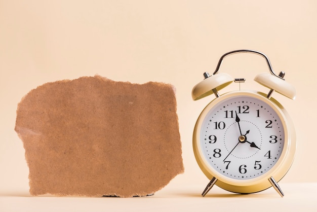 Blank brown torn paper near the alarm clock against colored background