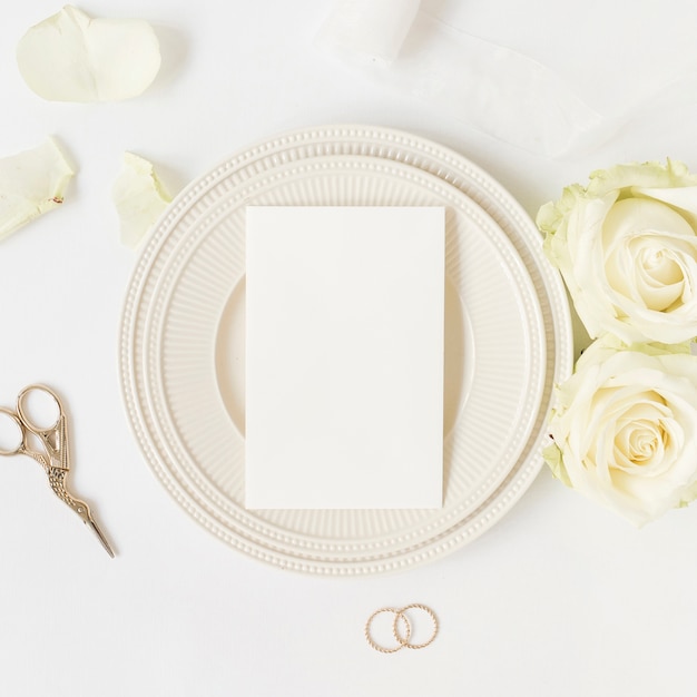 Free photo blank card on ceramic plate with roses; scissor and wedding rings on white background