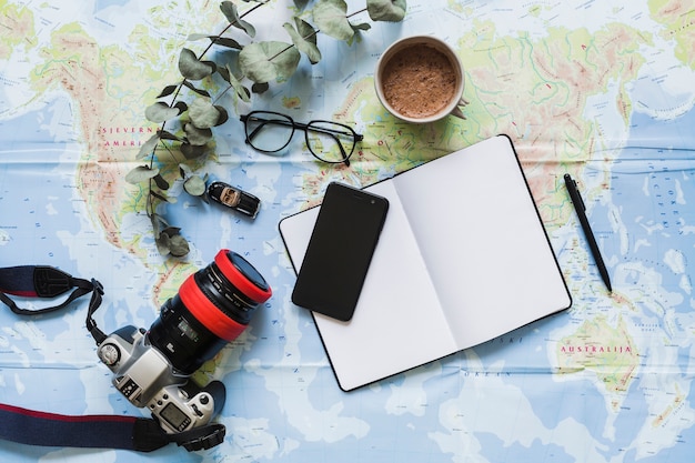 Blank diary, personal accessories, and coffee cup on the world map