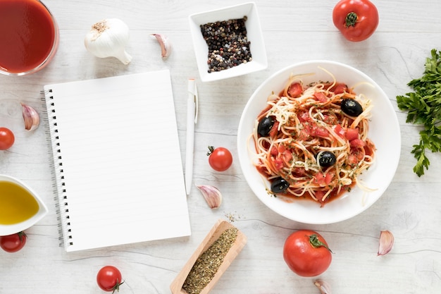 Free photo blank diary and yummy spaghetti pasta with fresh ingredient on white wooden table