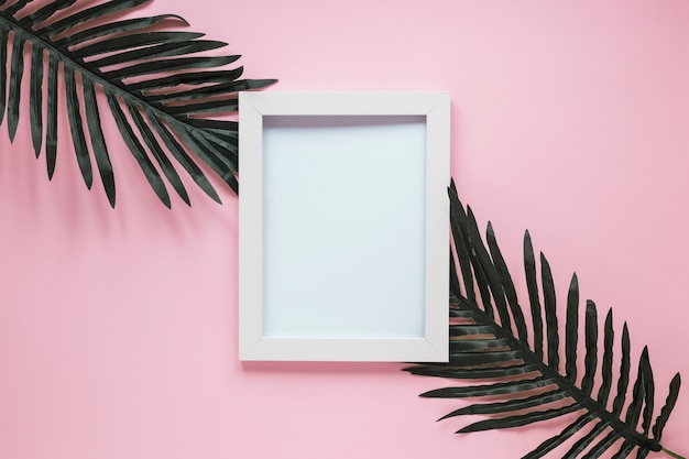 Blank frame with green leaves on table