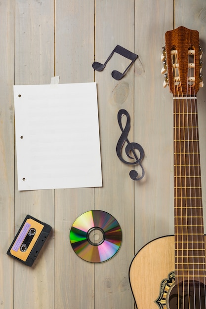 Free Photo blank musical page; cassette tape; compact disc; and musical note stuck on wooden wall with guitar