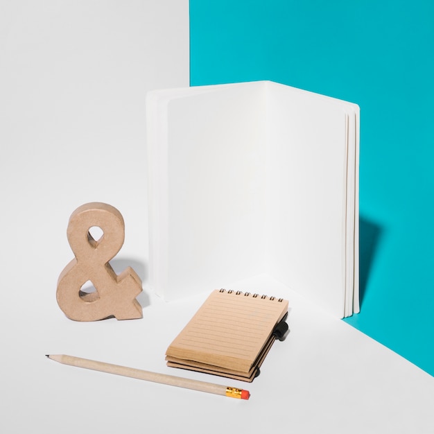 Free photo blank notebook; ampersand symbol; pencil; and spiral notepad on background