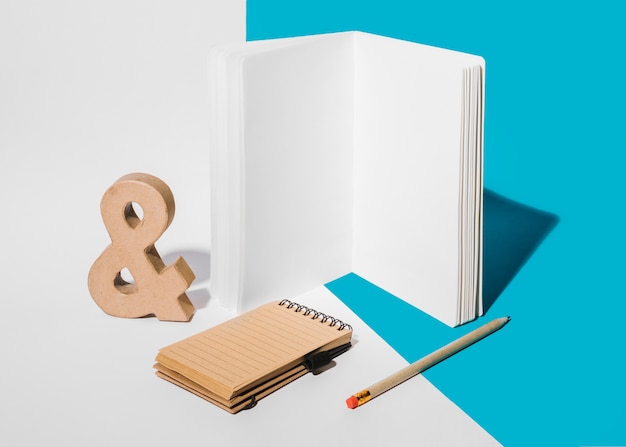 Blank notebook; ampersand symbol; pencil; and spiral notepad on white and blue background