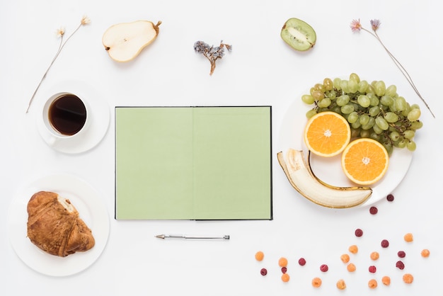 Blank open notebook with pen; croissant; coffee and fruits on white background