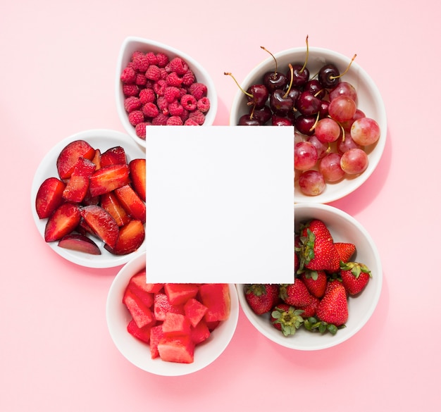 Blank page over the raspberries; plums; watermelon; strawberries; cherries; grapes and strawberries on pink background