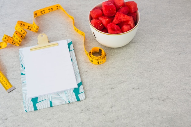 Free Photo blank paper attached on clipboard with measuring tape and watermelon cubes in the bowl